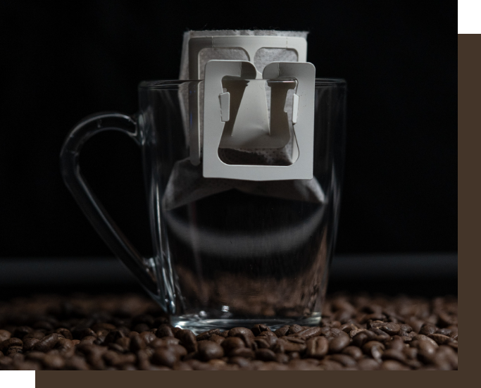 Puro Tinto single-serve drip coffee filter ready in a clear glass mug on a bed of roasted coffee beans